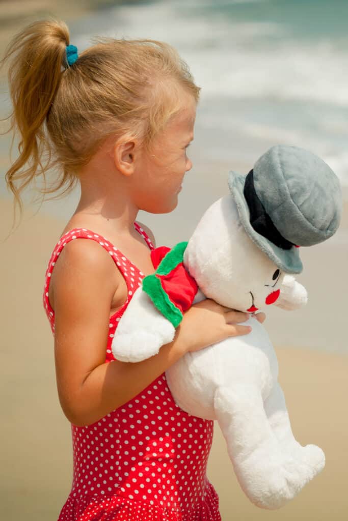 young girl holding a stuffed snowman standing on the beach