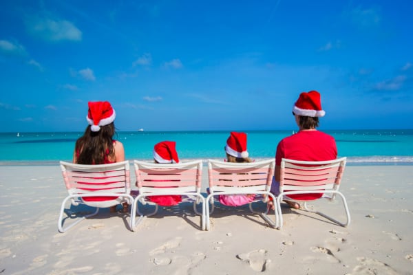 family sitting in beach chairs facing ocean wearing Santa hats