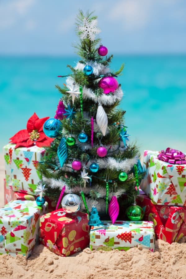 Small decorated Christmas tree on the beach with gifts underneath it