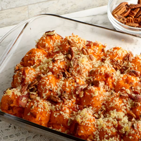 twice baked sweet potato casserole with bacon in baking dish next to a bowl of pecan halves