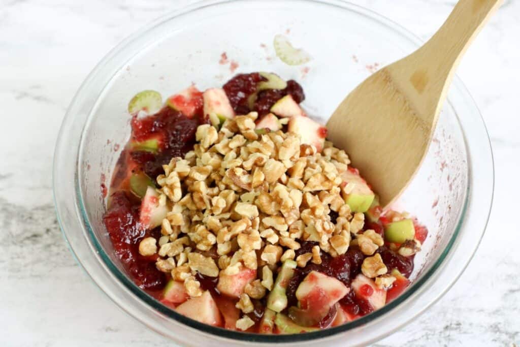 mixing nuts into a clear bowl of fruit and cranberry salad