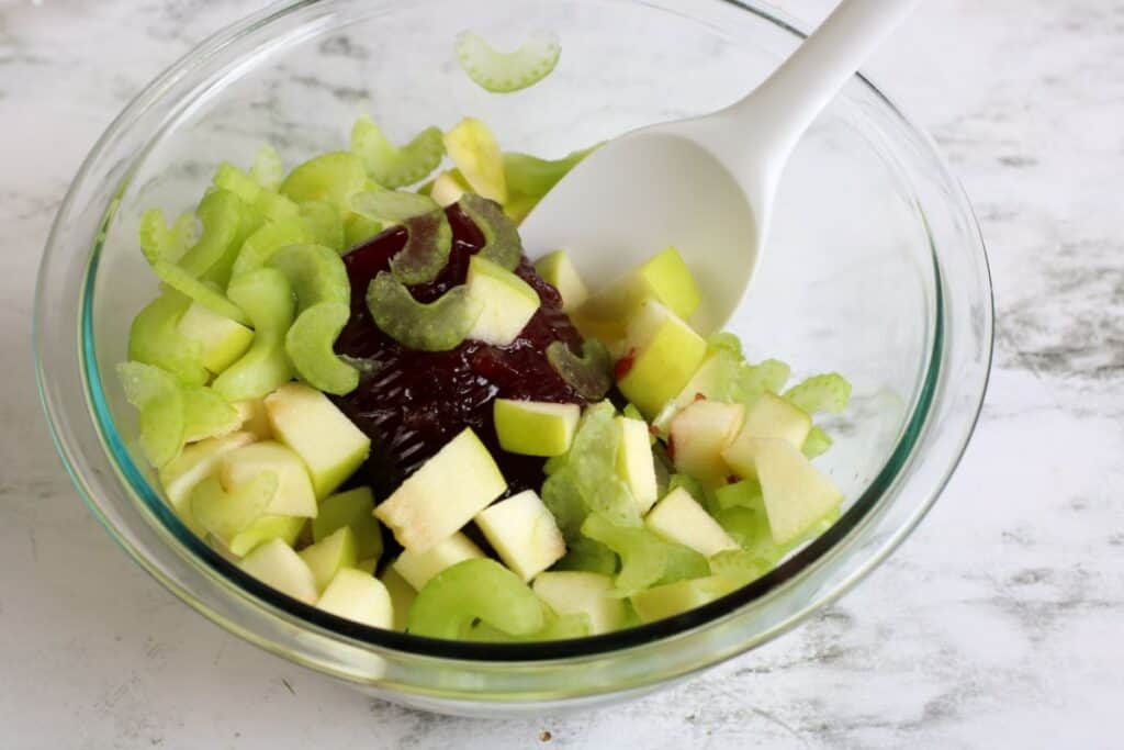 clear bowl of chopped green apples, cranberry sauce and celery