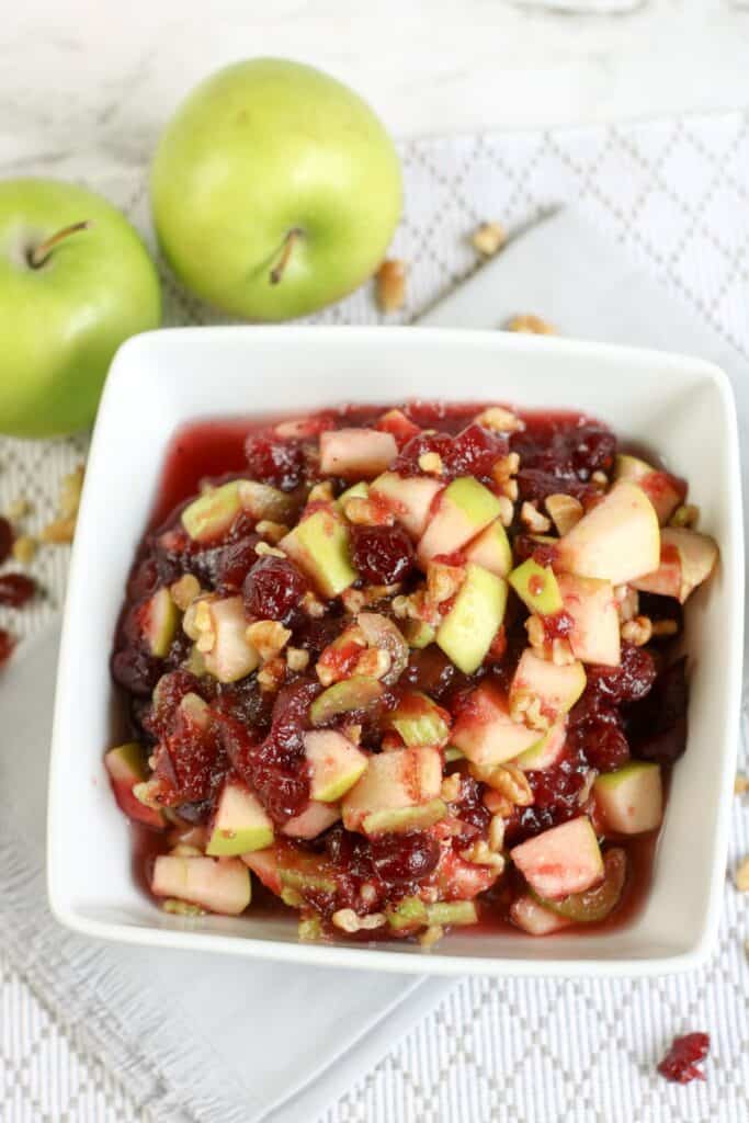 2 apples on a table with a bowl of apple cranberry salad