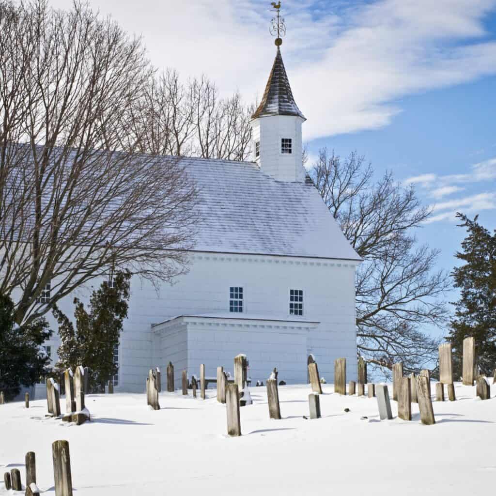 white church snow on ground next to cemetary